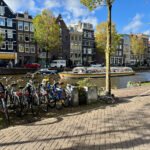 Amsterdam canal in the afternoon light, with calm water, narrow houses, and boats lining the edges.