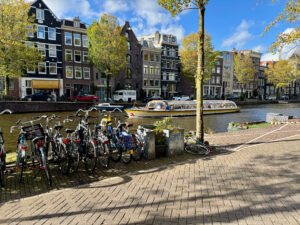 Amsterdam canal in the afternoon light, with calm water, narrow houses, and boats lining the edges.