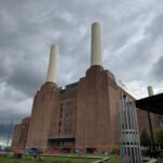 Battersea Power Station with four white chimneys towering over a riverside lawn filled with colourful deck chairs.