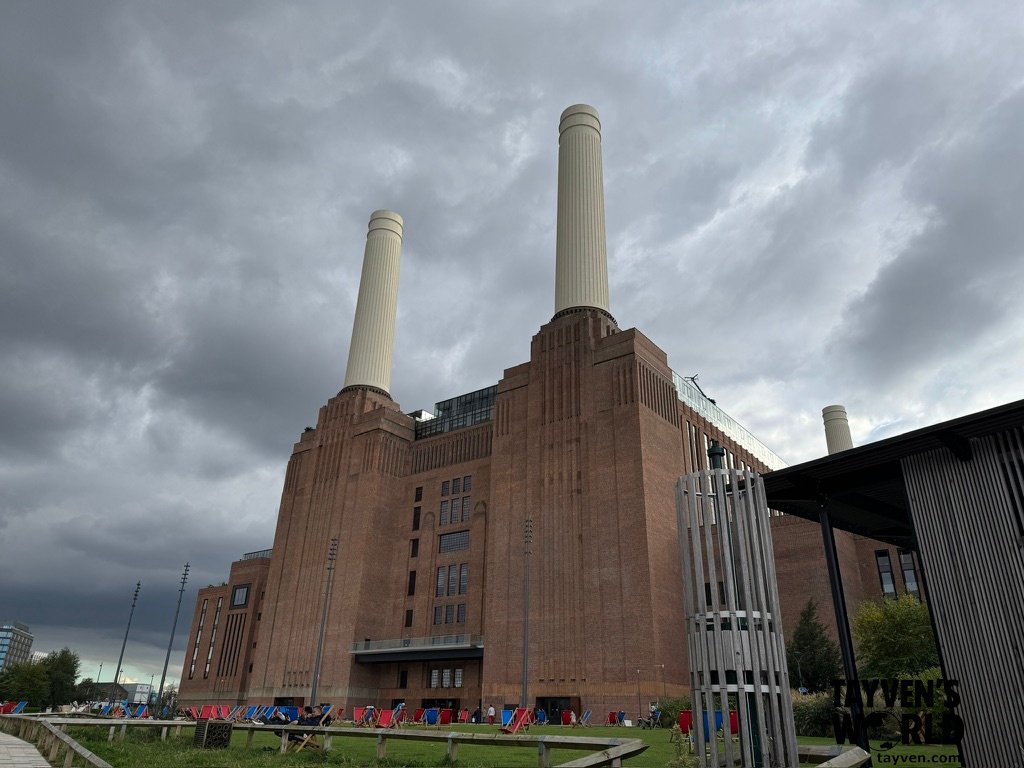 Battersea Power Station with four white chimneys towering over a riverside lawn filled with colourful deck chairs.