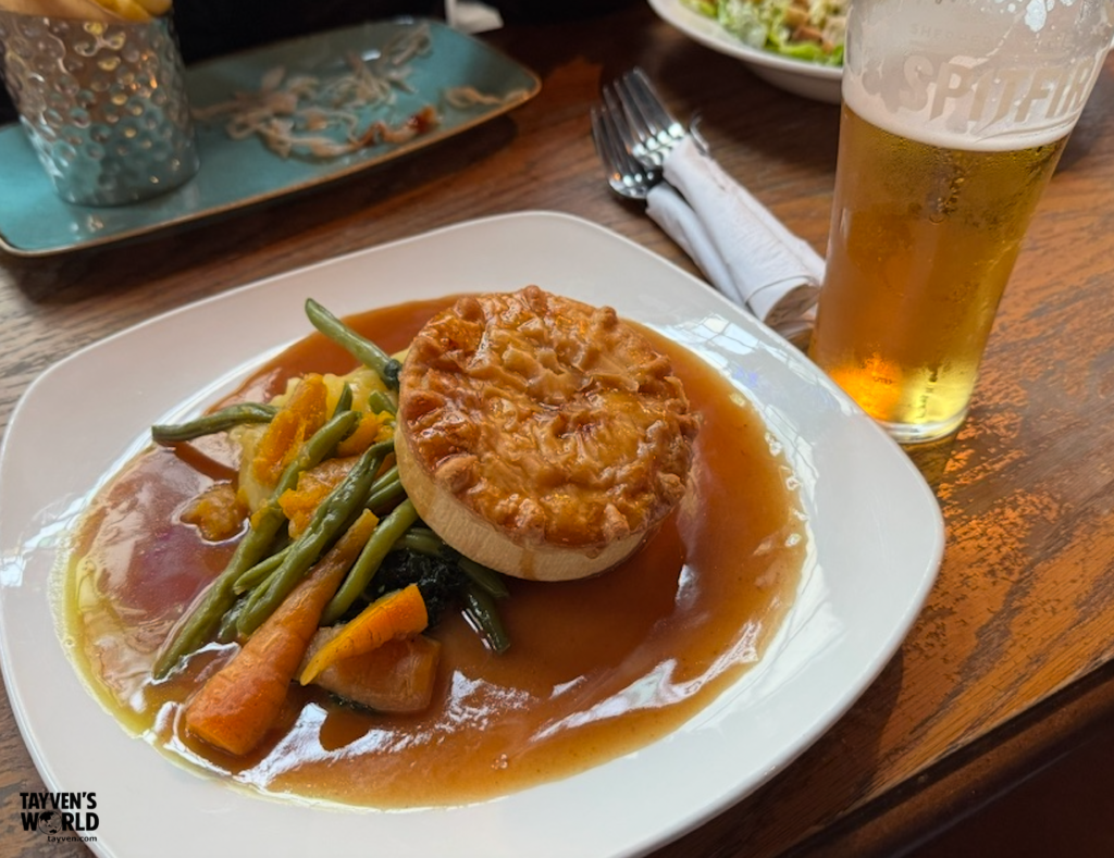 Plate of beef pie with vegetables and gravy served alongside a pint of Spitfire beer at The Bloomsbury Tavern in London.