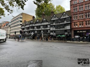 Street-level photo of a Tudor-style black‑and‑white timber‑framed building in London, with the Swan & Griffin signage, surrounded by modern shops and pedestrians on a wet pavement.