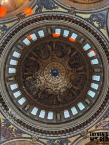 Upward-looking photo of the ornate dome inside St Paul’s Cathedral, showing sculpted figures, gilded details, frescoes, and windows illuminating the artwork.