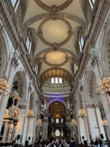 Interior photo of St Paul’s Cathedral showing ornate arches, chandeliers, and the richly decorated central dome with visitors gathered below.