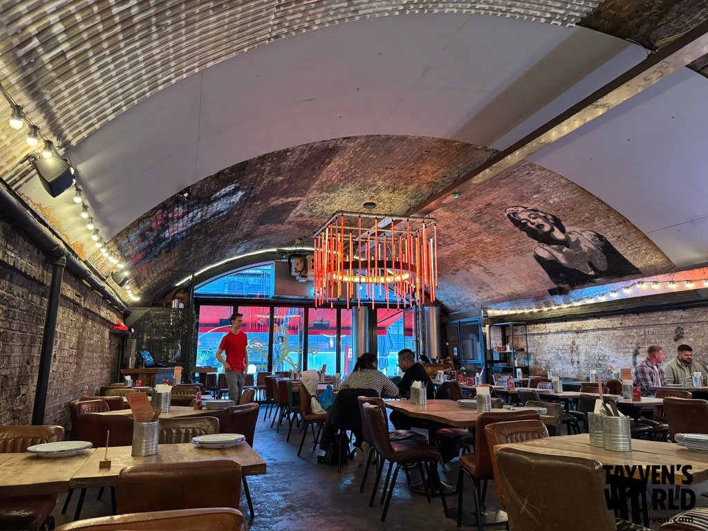 Interior of Gordon Ramsay’s Street Pizza at Battersea, with exposed brick arches, warm lighting, and diners seated at wooden tables.