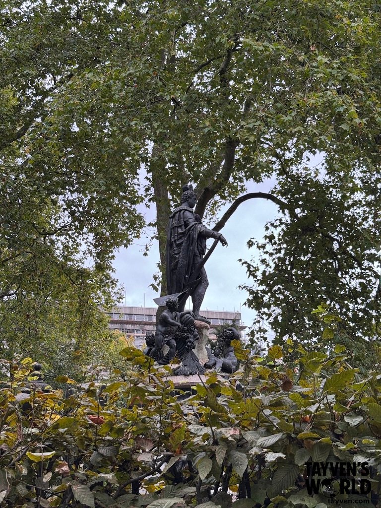 Bronze Garden Statue Bronze statue surrounded by trees and greenery in an outdoor garden area.