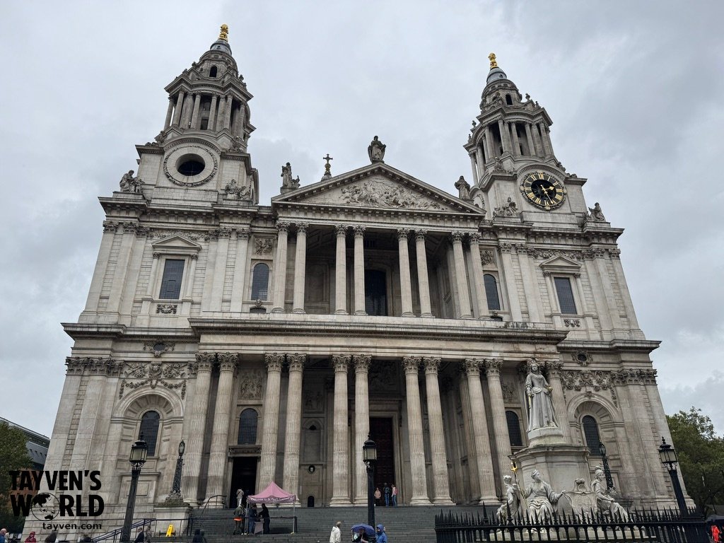 Wide-angle photo of the front entryway of St Paul’s Cathedral in London, showing the stone steps leading up to the large wooden doors and the symmetrical twin towers above.