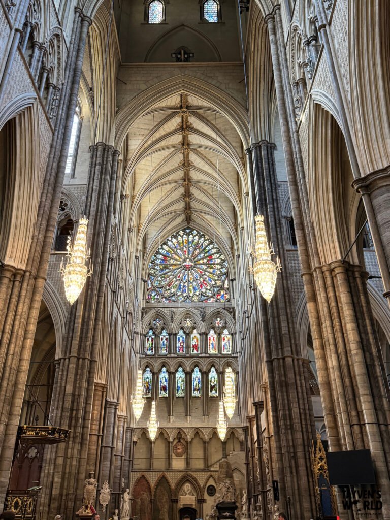Interior of Westminster Abbey’s nave with soaring Gothic arches, ribbed vaults, chandeliers, and the Great West Window glowing above the apse.