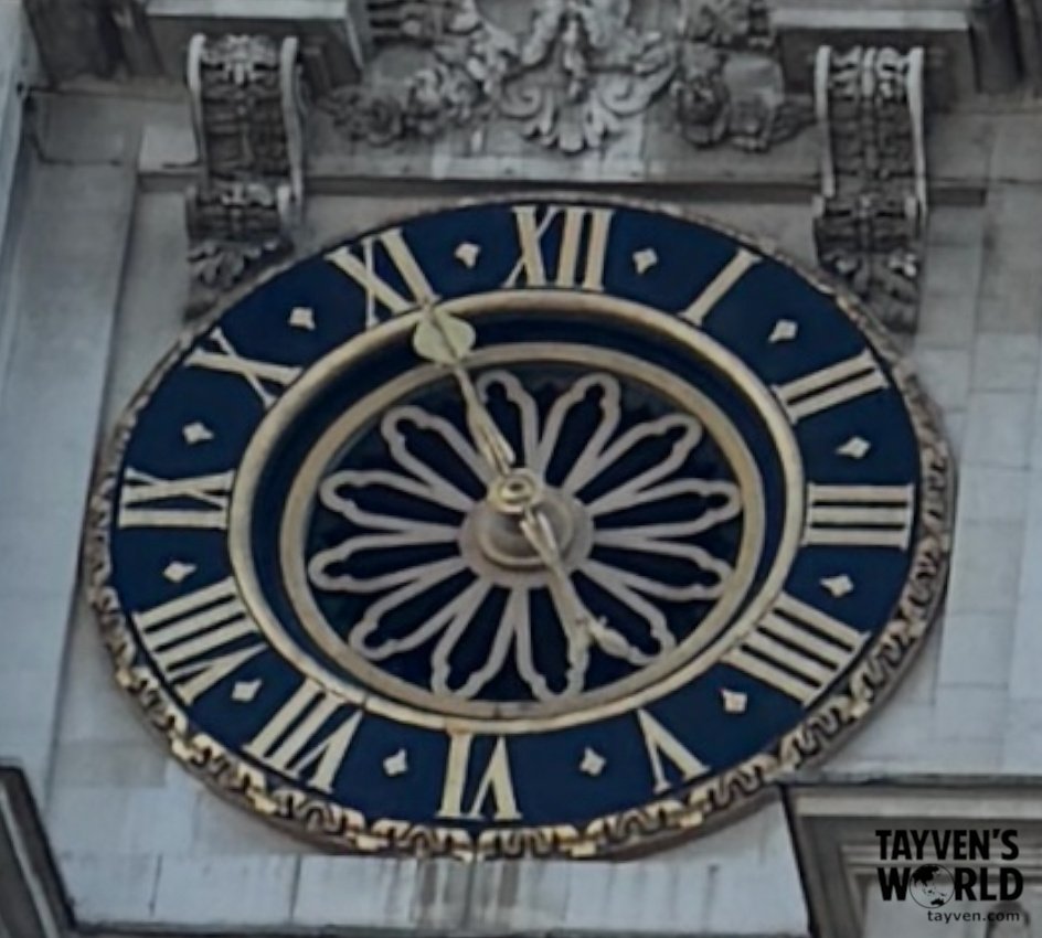 Blue and gold clock mounted on an ornate stone building, showing the time at around 11:25.