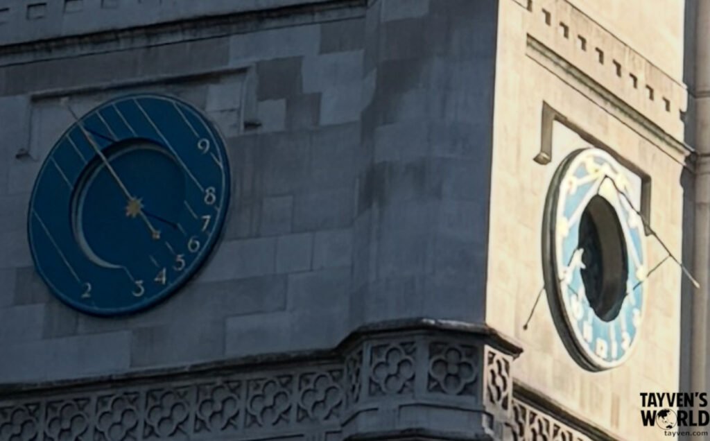 Two decorative blue clock faces on a stone tower, each with unique numbering and ornate detailing.