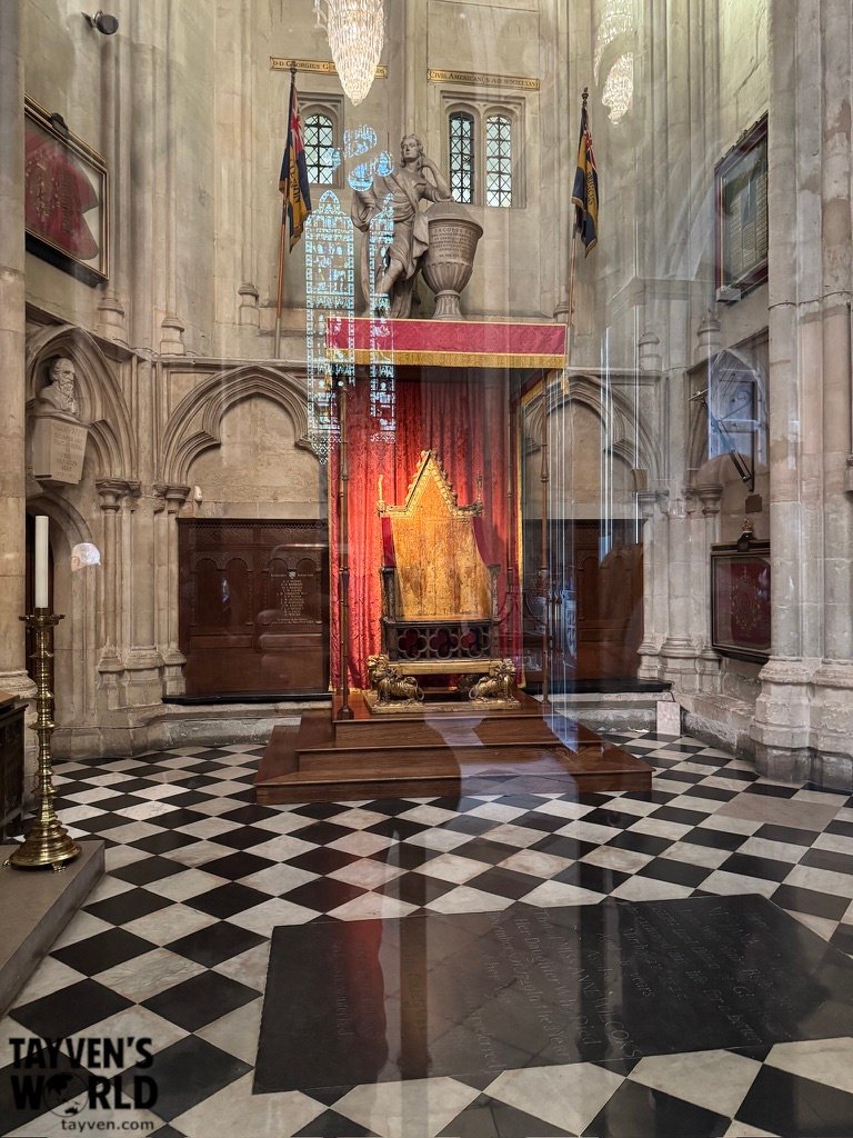 The Coronation Chair inside Westminster Abbey, displayed beneath a red and gold canopy with carved lions at its base.