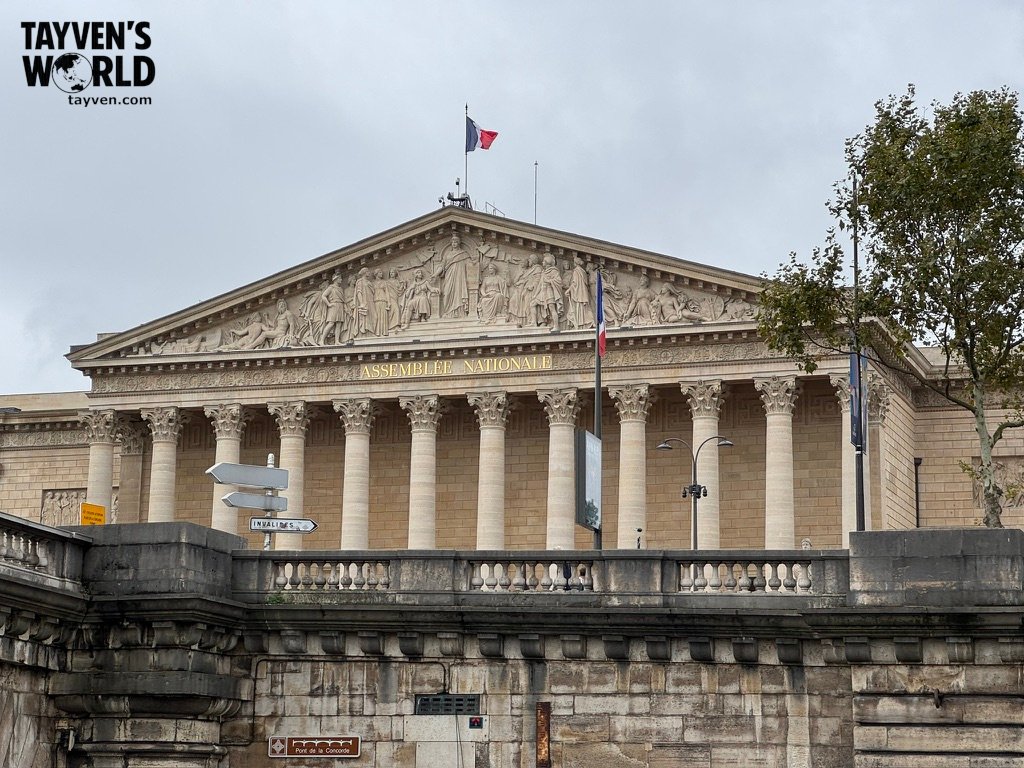 Neoclassical façade of the Assemblée Nationale with French flags and gold lettering above Corinthian columns.