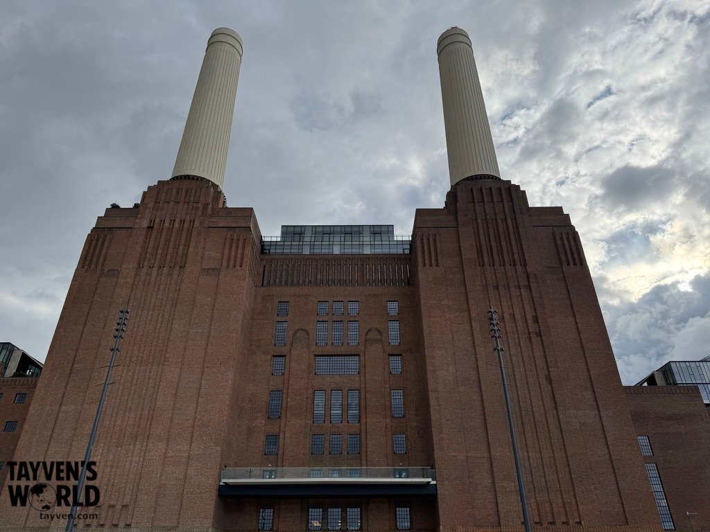 Battersea Power Station with two restored chimneys rising above the brick façade under a cloudy London sky.