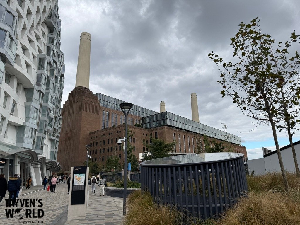 Pedestrian walkway behind Battersea Power Station with landscaped paths and modern apartment buildings near the Tube station.