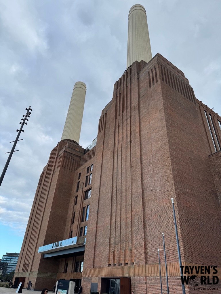 Close view of Battersea Power Station’s brick façade and two tall chimneys against a cloudy sky.
