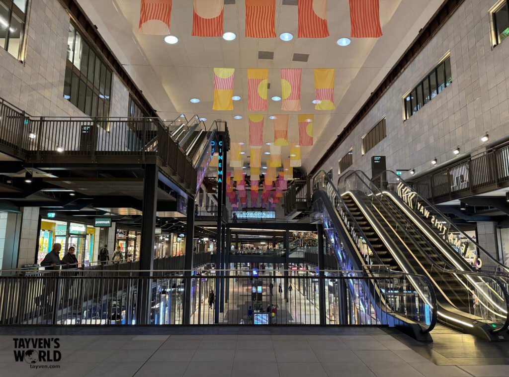 Multi‑level interior of Battersea Power Station with escalators, colourful hanging banners, and a cinema sign.