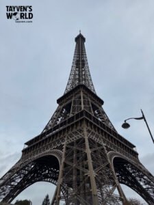 Low‑angle view of the Eiffel Tower showing its iron lattice structure against an overcast sky.