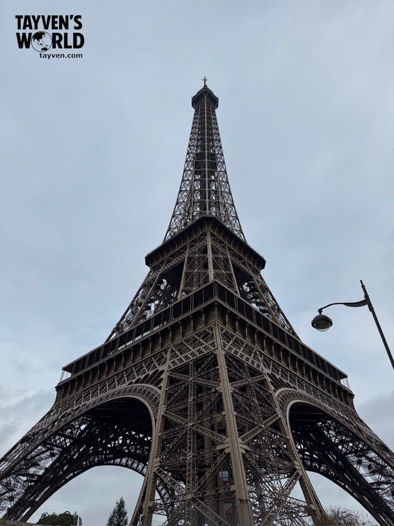 Low‑angle view of the Eiffel Tower showing its iron lattice structure against an overcast sky.