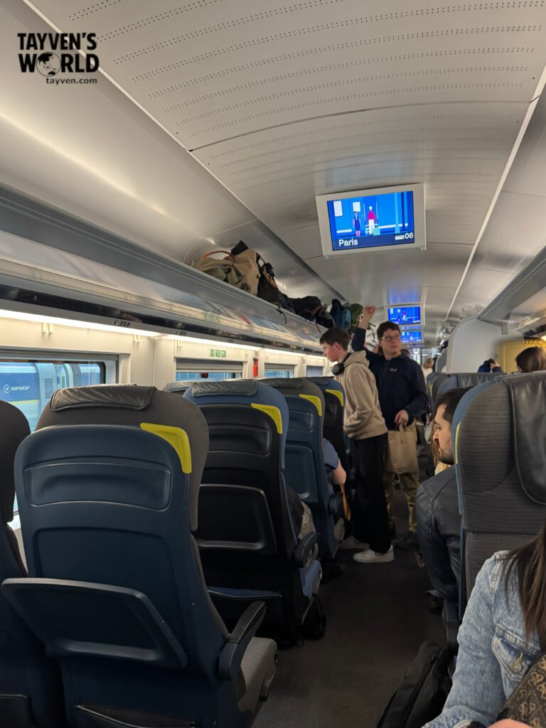 Passengers seated inside Eurostar train with digital screen showing Paris destination.