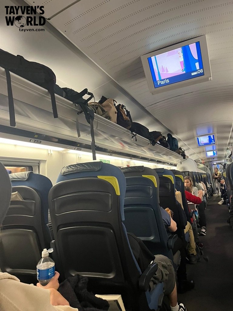 Passengers seated inside Eurostar carriage with overhead luggage racks and digital screens showing Paris destination.