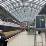 Eurostar train under glass roof at St Pancras with station clock and passengers.