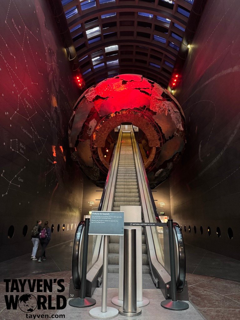 Escalator leading through a giant illuminated globe inside the Earth Hall at the Natural History Museum in London.