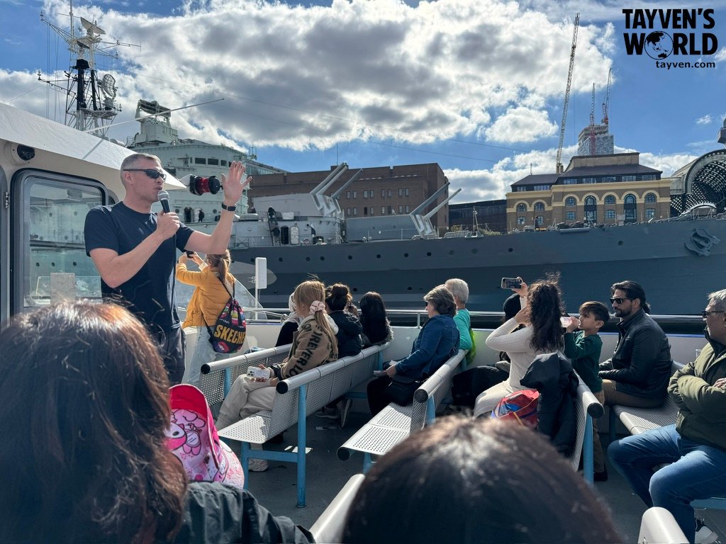 Tour guide speaking to passengers aboard a City Cruises boat on the River Thames.