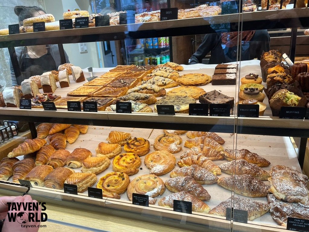 akery display case filled with croissants, pastries, cookies, and cakes labeled with prices.