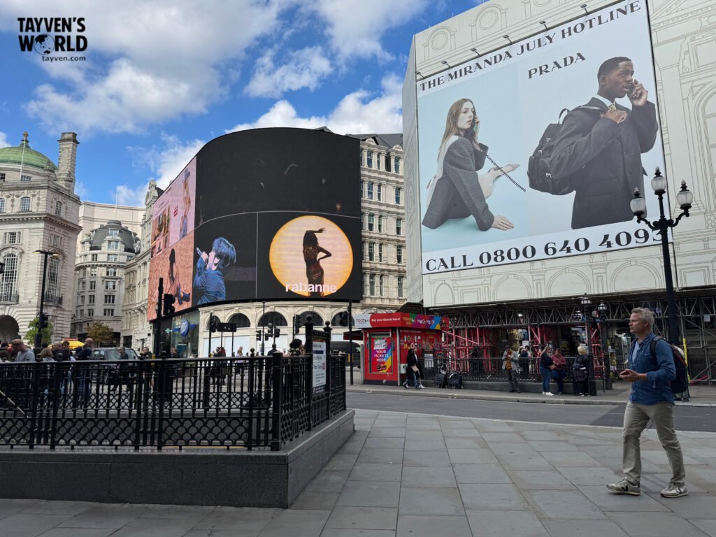 Piccadilly Circus with digital billboards and pedestrians under a partly cloudy sky.