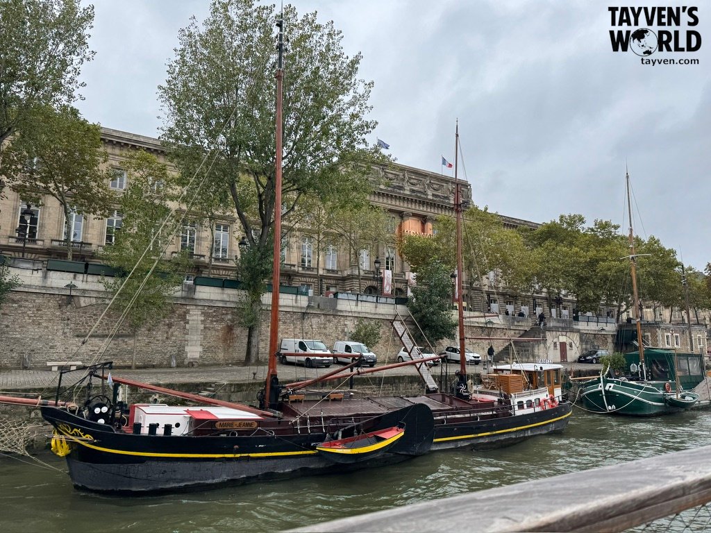 Traditional boats moored along the Seine River near historic Parisian buildings and trees.