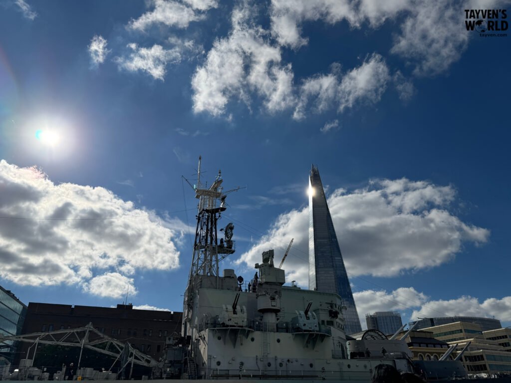 HMS Belfast warship docked on the Thames with The Shard rising behind it.