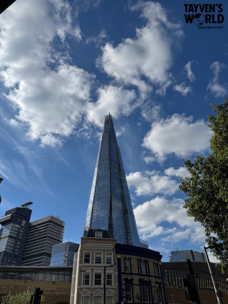 The Shard viewed from street level surrounded by modern and historic buildings under a bright sky.