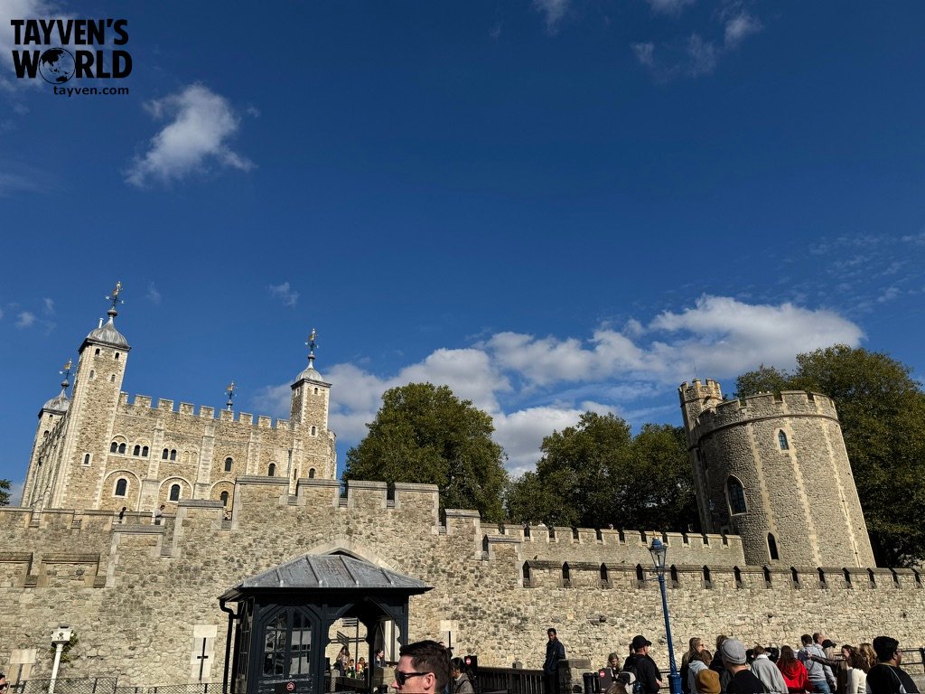 The Tower of London fortress with stone walls and towers under a bright blue sky.