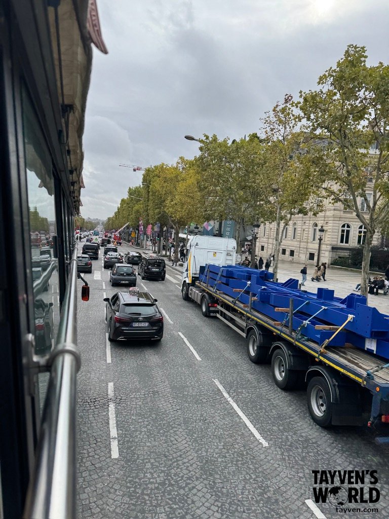View of Paris traffic from the upper deck of a bus along a tree‑lined avenue.