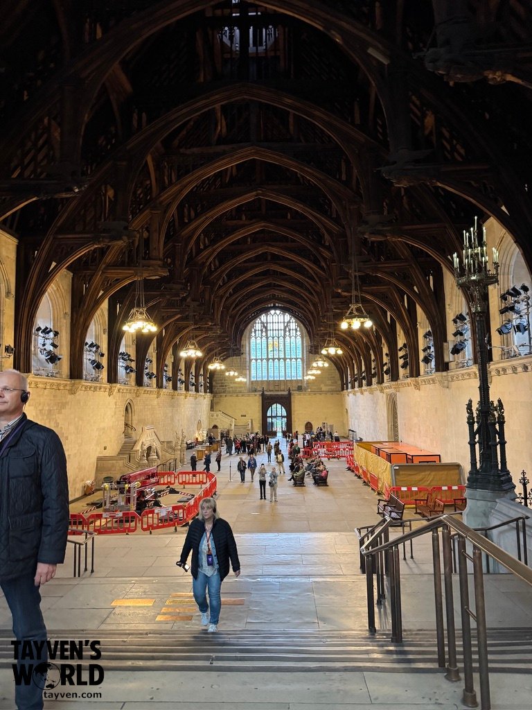 Interior of Westminster Hall showing its vast timber‑vaulted ceiling, stone walls, and visitors exploring the historic space.