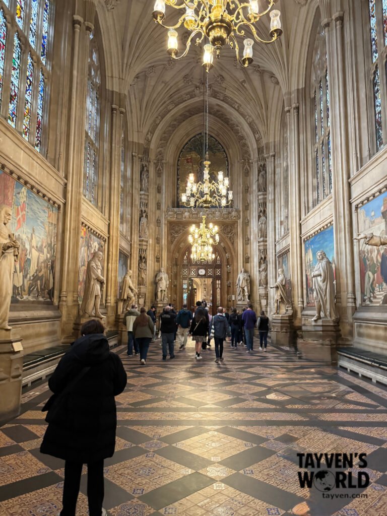 Visitors walking through Westminster Hall with chandeliers, statues, and murals.
