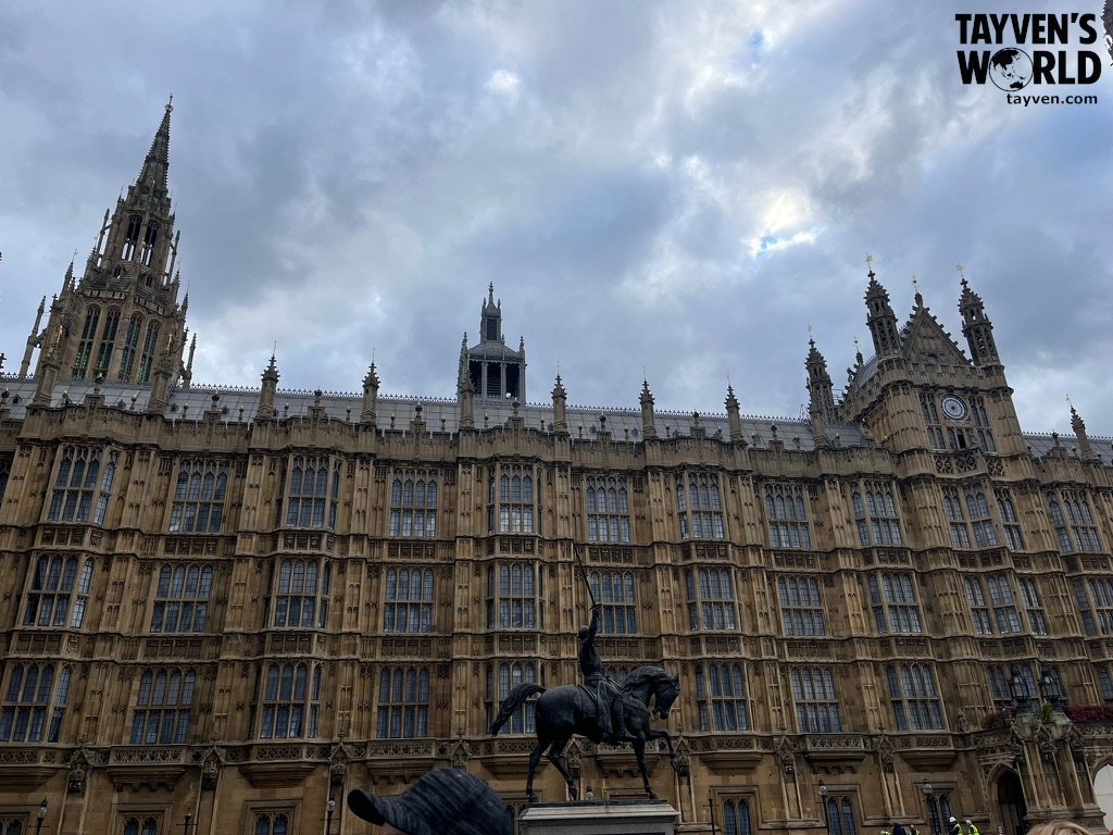 Palace of Westminster façade with equestrian statue under cloudy sky.