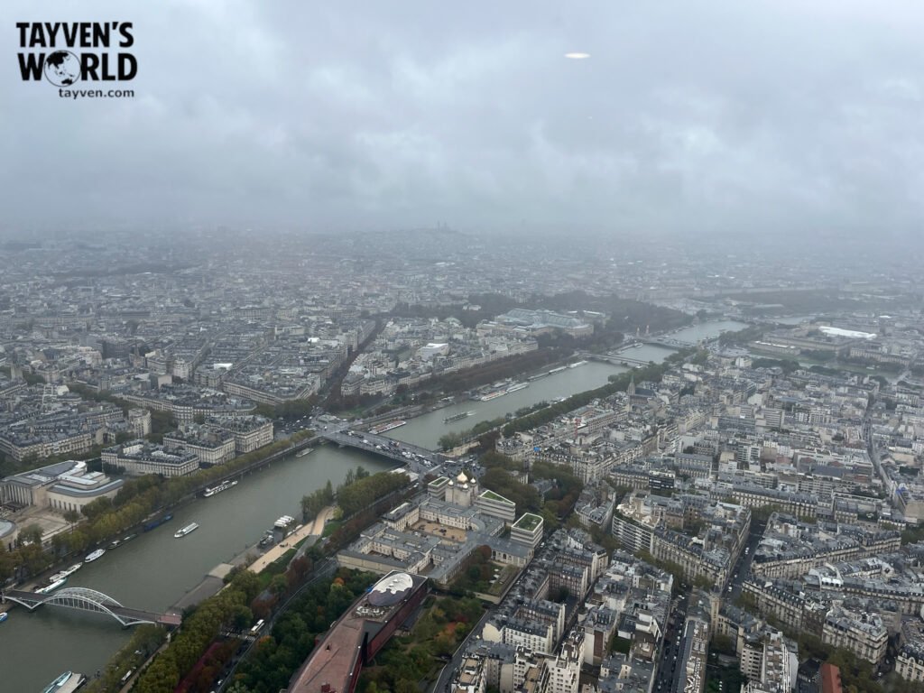 Misty aerial view of Paris from the Eiffel Tower showing the Seine River and city rooftops.