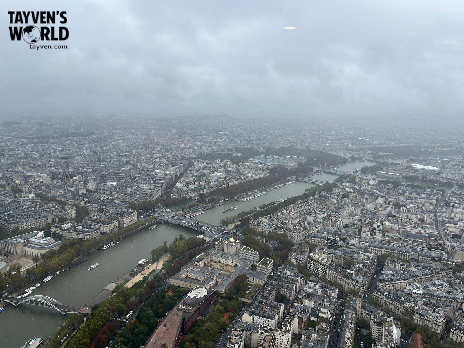Misty aerial view of Paris from the Eiffel Tower showing the Seine River and city rooftops.
