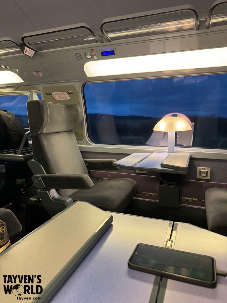 First‑class train cabin with soft seats, fold‑out tables, and a warm reading lamp.