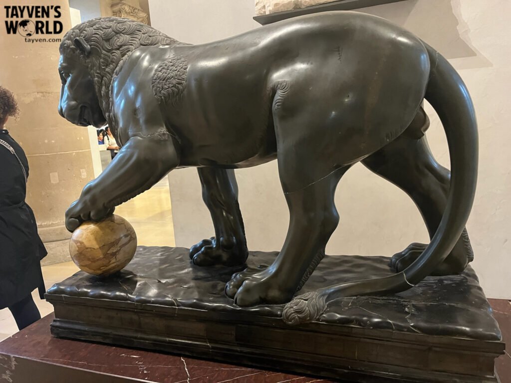 Stone lion sculpture with paw resting on a marble sphere in the Louvre Museum.
