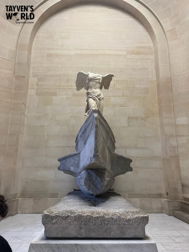 The Winged Victory of Samothrace statue displayed on a stone ship base at the Louvre Museum.