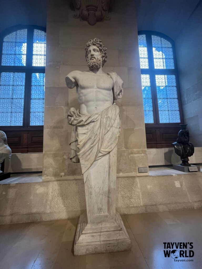 Marble statue of a bearded Roman figure displayed in the Louvre Museum.