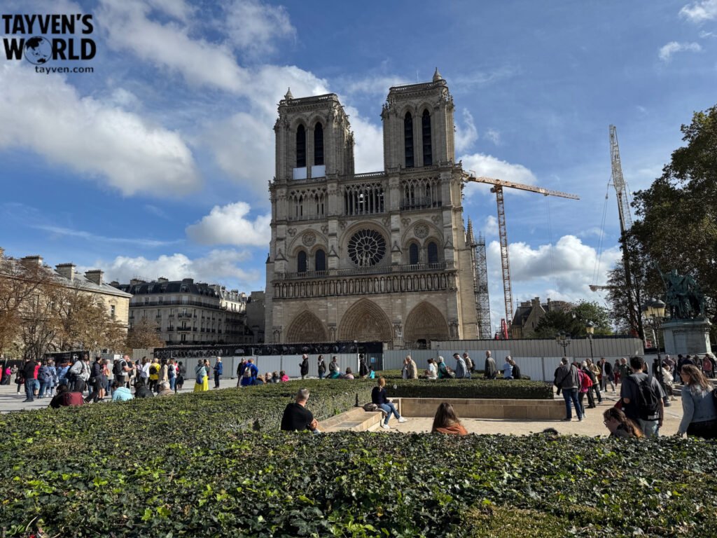 Front façade of Notre‑Dame Cathedral with crowds and restoration cranes.