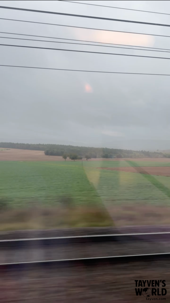 Overcast farmland seen through train window with power lines overhead.