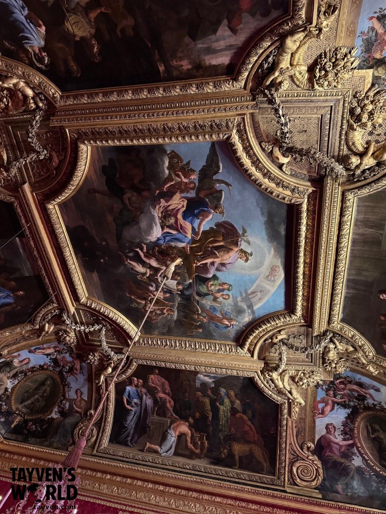Ornate painted ceiling with gilded frames and mythological scenes at Versailles.