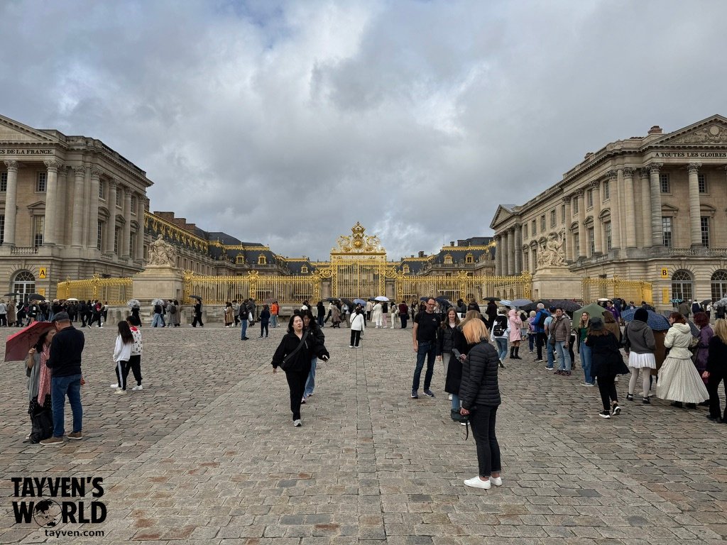 Visitors gathered in the cobblestone courtyard before the golden gates of Versailles.