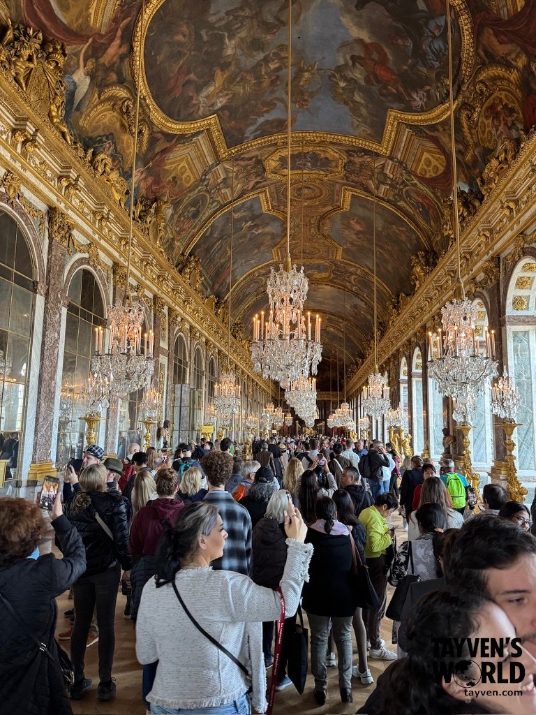 Tourists walking through the Hall of Mirrors surrounded by chandeliers and gilded décor.