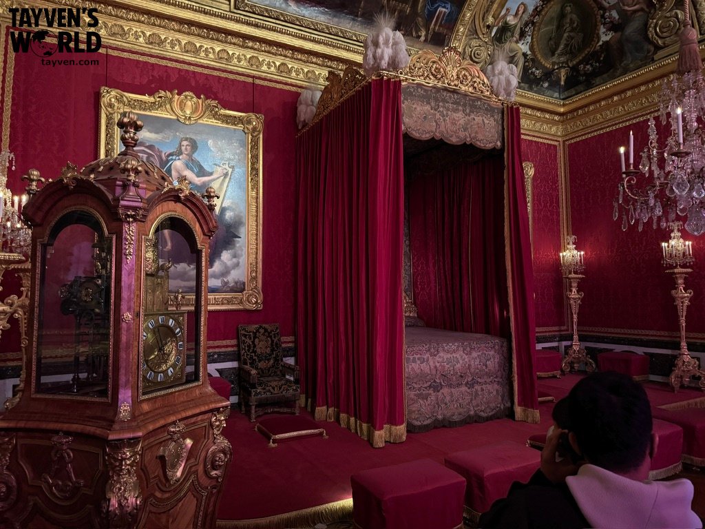 Ornate red and gold royal bedroom with canopy bed and antique clock at Versailles.