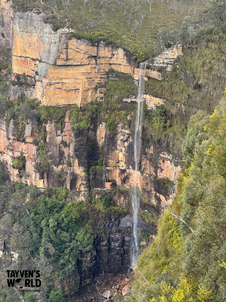 Wide view of Govetts Leap showing the Grose Valley, sandstone cliffs, and distant waterfall under a cloudy sky.